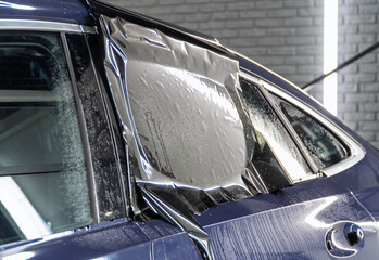 Male car service worker glue window tinting in luxury car detailing car repair the concept of love for cars and protection. Applying tinting foil on a car window in the tuning studio close-up. 