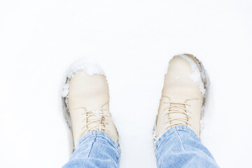 Women legs close-up in blue jeans and white boots standing on white snow in winter park. Walking in nature concept. High quality photo