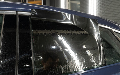 Male car service worker glue window tinting in luxury car detailing car repair the concept of love for cars and protection. Applying tinting foil on a car window in the tuning studio close-up. 