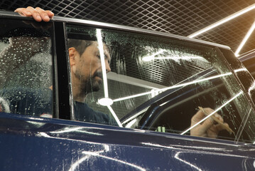 Male car service worker glue window tinting in luxury car detailing car repair the concept of love for cars and protection. Applying tinting foil on a car window in the tuning studio close-up. 