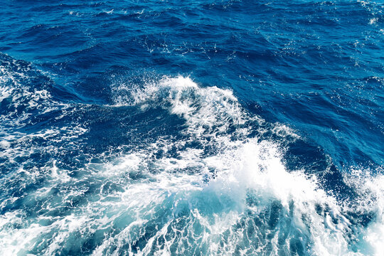 Vibrant ocean waves crashing against blue surface on a sunny day