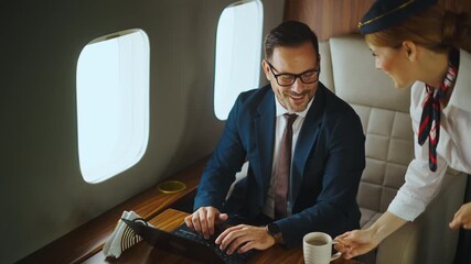Confident middle-aged businessman working on his laptop while traveling in a private jet, when a flight attendant brings him coffee and he takes a sip before continuing to work - Powered by Adobe