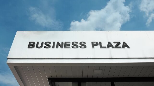 Business Plaza word sign prominently displayed on the modern, commercial facade of a complex beneath a clear blue sky, signifying a landscaped area or multi-tenant building housing various offices