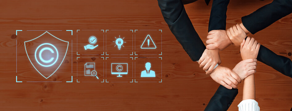 A top-down view of diverse hands joining together symbolizes teamwork and unity in the context of copyright protection, featuring legal icons on a wooden desk. Trope