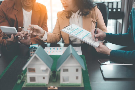 A group of young Asian businesspeople meet at an office for a residential real estate project. A group of elegant, professionally dressed individuals evaluate a small house model. - Powered by Adobe