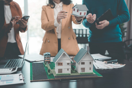 A group of young Asian businesspeople meet at an office for a residential real estate project. A group of elegant, professionally dressed individuals evaluate a small house model.