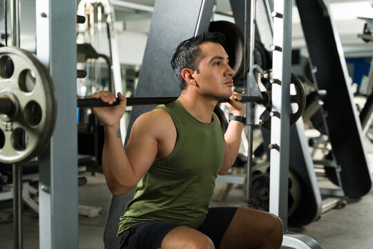 Strong Latin man doing squats in fitness gym