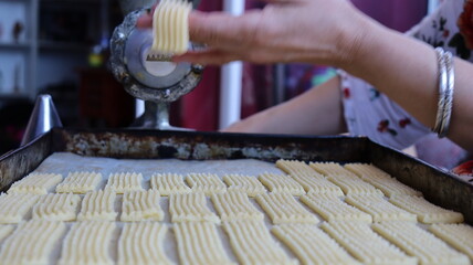 Halwa Lbouq (Moroccan Horn Pastry) - Batch of Sesame-Coated Pastries Ready to Bake, Woman Shaping Raw Dough with Traditional Cookie Press, Silver Bracelets, Home Baking Setup for Eid/Ramadan