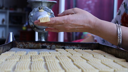 Halwa Lbouq (Moroccan Horn Pastry) - Batch of Sesame-Coated Pastries Ready to Bake, Woman Shaping Raw Dough with Traditional Cookie Press, Silver Bracelets, Home Baking Setup for Eid/Ramadan