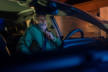 Man fastening seat belt in car at night, ensuring safety while driving.