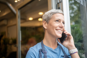 Smiling female florist talking on phone taking flower orders from customers in her small business flower shop.