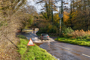 Car driving through flooded country lane after heavy rain