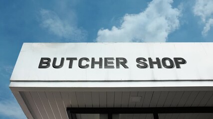 Butcher Shop word sign plainly displayed on the commercial facade of a retail building beneath a bright blue sky, signifying a location specializing in cutting, preparing, and selling meat products
