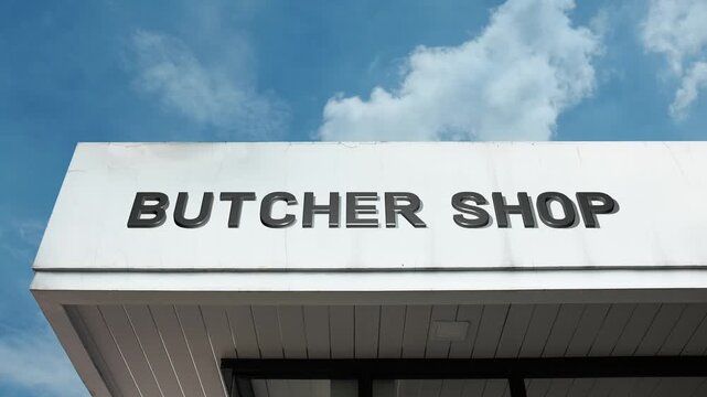 Butcher Shop word sign plainly displayed on the commercial facade of a retail building beneath a bright blue sky, signifying a location specializing in cutting, preparing, and selling meat products