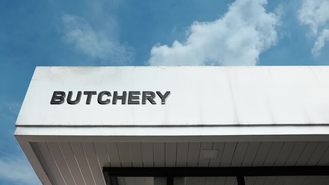 Butchery word sign plainly displayed on the commercial facade of a retail building beneath a bright blue sky, signifying an establishment specializing in the preparation and sale of meat and meat