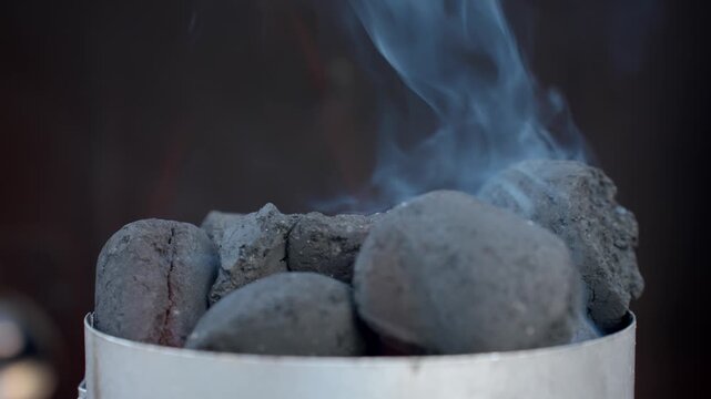 Close-up of charcoal briquettes smoking inside metal grill starter. Concept of barbecue preparation, outdoor cooking and summer picnics