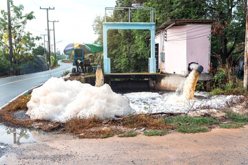 Murky foam piles created by floating fast from flow of polluted water from a large water pump to accelerate drainage after rain at irrigation canal gate along village road in rural Thailand.
