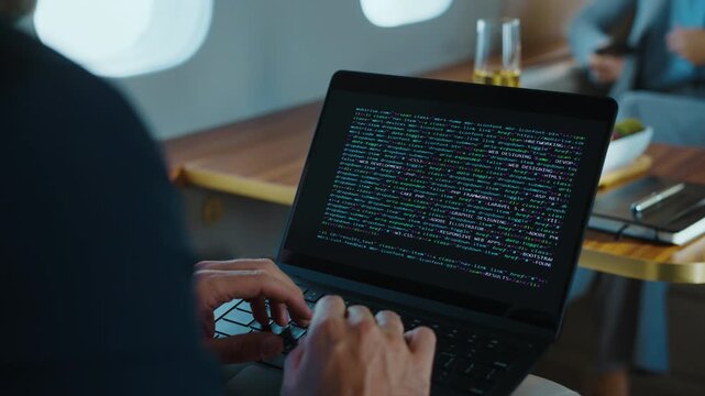 Focused programmer diligently typing code on a modern laptop, working on a complex software project while traveling in the luxurious first-class cabin of a private airplane - Powered by Adobe