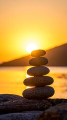 Stacked stones in balance against a golden sunset over water