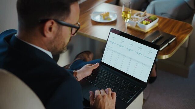 Successful manager analyzing financial data on a spreadsheet while traveling in a first class airplane cabin, enjoying a comfortable and luxurious business trip with champagne and appetizers