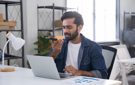 Indian man using AI voice assistant on smartphone in office, interacting with virtual assistant app for productivity, AI-powered speech, and smart technology.
