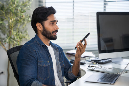 Indian man using AI voice assistant on smartphone in office, interacting with virtual assistant app for productivity, AI-powered speech, and smart technology.