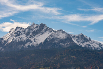 Snow-capped mountain peak under bright blue sky with patchy clouds.