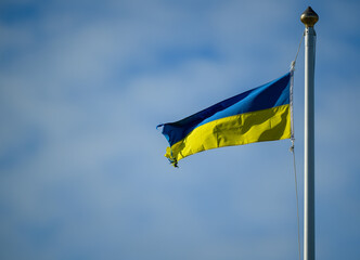 A vibrant Ukrainian flag is flying proudly on a flagpole against a bright blue sky. The colors blue and yellow vividly represent the nation's identity and heritage
