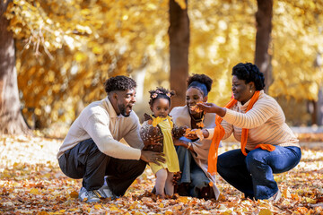 African American Family Walking and Collecting Leaves in Autumn Park