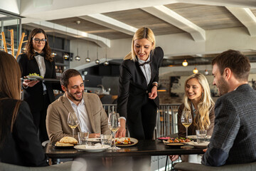 Restaurant staff serving food to happy customers at a stylish dining table