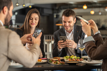 Friends enjoying a meal at a restaurant while using their smartphones