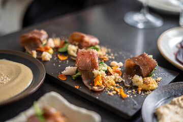 Gourmet dish of cured meat with vegetables and sauce on a dark plate