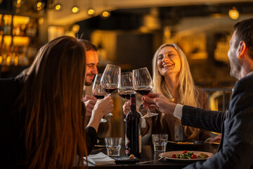 Friends toasting with red wine at a restaurant, celebrating a special occasion