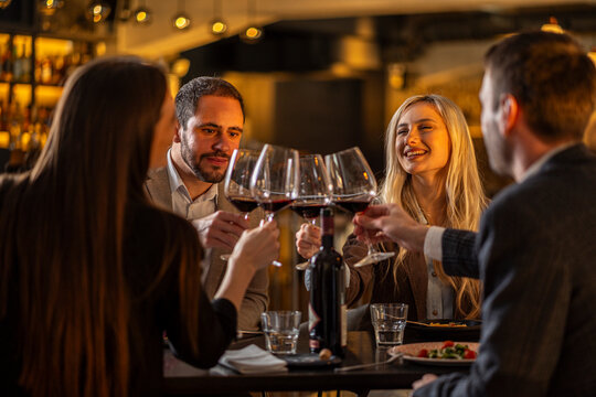 Friends toasting with red wine at a restaurant, celebrating a special occasion.