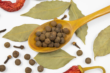 A spoon with allspice and spices on a white background.