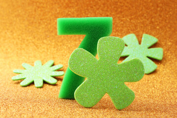 Luck and prosperity, number seven surrounded by flowers with a hopeful green color on a gold background