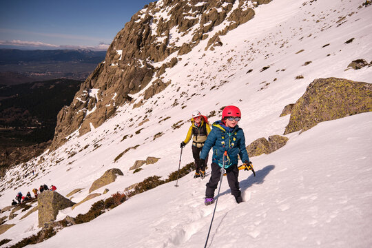 Family walking down a snowy slope, carrying mountaineering equipment