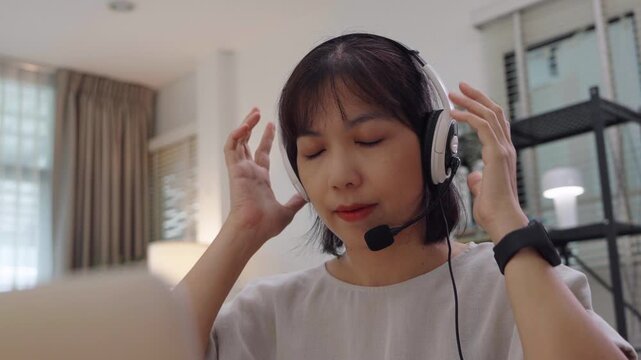 Young Asian girl carefully adjusting her headset microphone while getting ready for an online lesson at home, staying focused and preparing to join her virtual class.