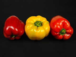 Three bell peppers, yellow, orange and red are on a black table