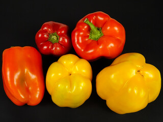 Yellow, orange and red bell peppers are on a black table, rich crop of vegetables
