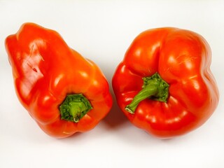 Two red bell peppers of different shapes and size are on a white board, autumn composition
