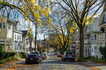 Quiet suburban street lined with parked cars, houses, and trees on a beautiful autumn day in Brighton, Boston, Massachusetts, USA  © Baharlou