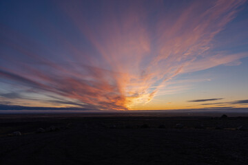 Colorful clouds streak across the horizon at sunset, over a barren landscape.