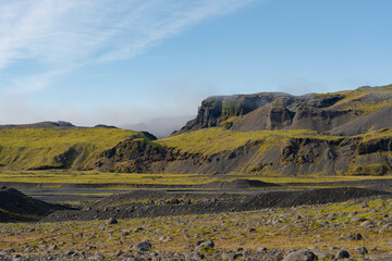 Scenic landscape with rocky hills, green moss, and clear blue sky above.