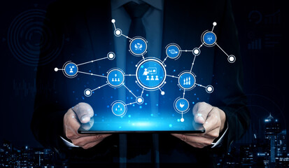 A businessman in a suit holds a tablet displaying glowing digital network connections, symbolizing data analysis and modern technology in a business context. Tessel
