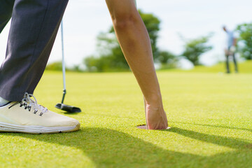 Golfer retrieving ball from hole on green in morning.