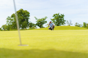 Senior Asian golfer lining up a putt on green. Senior activity.