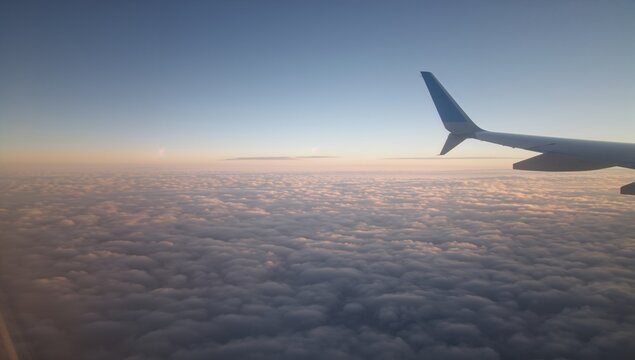 Airplane Window View Above Snowy Clouds, soft pale winter sunlight illuminating white clouds below, peaceful and dreamy aerial travel visuals 