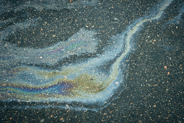 Iridescent oil spill creating abstract rainbow pattern on asphalt.