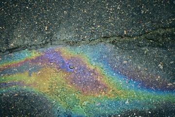 Oil slick spreading on wet asphalt, creating a vibrant colorful iridescent surface.